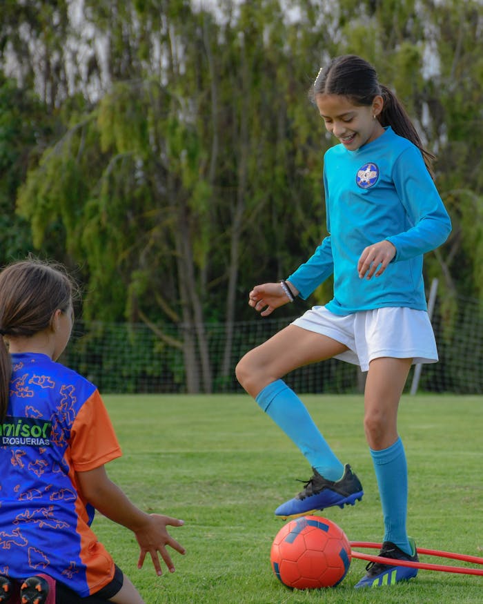 Two young girls enjoying soccer practice outdoors on a bright day.